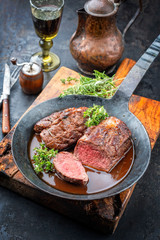 Traditional barbecue aged saddle of venison with herbs game sauce as closeup in a wrought iron...
