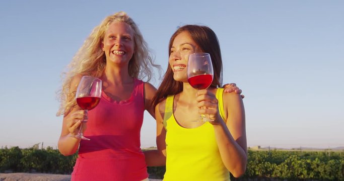 Friends drinking red rose wine at vineyard wine tasting - women having fun. Happy women holding glasses of red wine or rose enjoying a glass outside at sunset.
