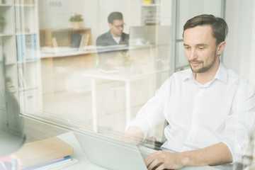 Fototapeta premium Serious manager sitting in white shirt busy with his work, he typing on laptop at his workplace at office