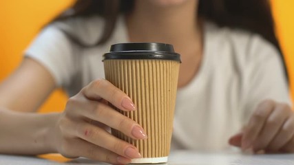 Female drinking hot beverage from carton cup during coffee break, hand close-up