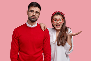 Excited pretty woman in white shirt raises palm, keeps hand on shoulder of friend who has sad...