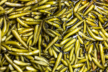 Marinated green peppers in water on the counter in the supermarket. Glare around the peppers.