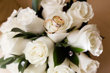 A pair of wedding rings on a bouquet of white roses, close up shot