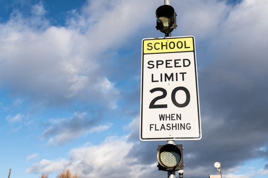 Speed limit 20 when flashing sign near school. Cloudy sky in the background.