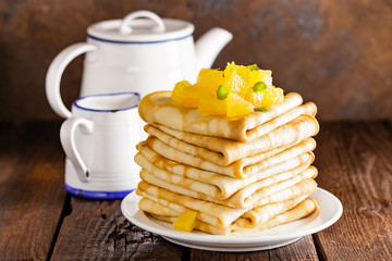 Homemade thin crepes with orange jam, stack of pancakes on wooden rustic background