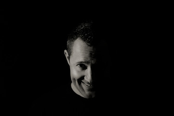 Face of a shy smiling man in black and white low key portrait