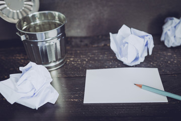 garbage bin on desk setting with empty notepad and scrunched paper balls