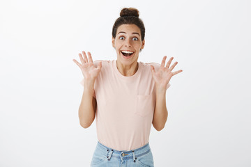 Happy excited attractive female in t-shirt with messy bun hairstyle raising palms near shoulders...