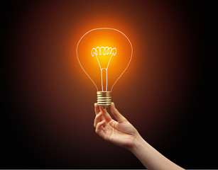 Hand holding light bulb on dark background, new idea concept