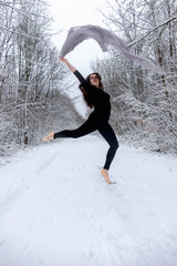 Junge schöne Frau Mädchen braunhaarig in schwarzem Ballett Anzug springt und tanzt Spitze im verschneiten Winter Wald 