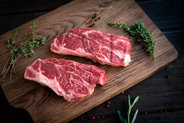 Raw chuck roll steaks premium beef with seasonings on wooden board, top view, rustic stule
