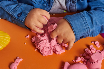 The hands of a child playing with kinetic sand. Close up. Orange background