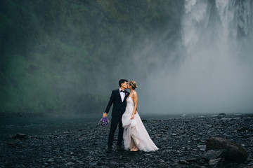 Young happy wedding couple kissing on background of waterfall, outdoors