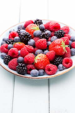 Fresh berry salad on blue dishes. Vintage wooden background.