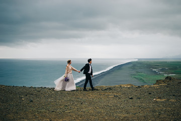 Young wedding couple walking outdoors on background of mountain landscape and ocean with black beach