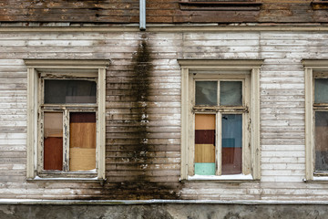 Old, abandoned wooden house wall with windows and cracked paint. Close-up photo.