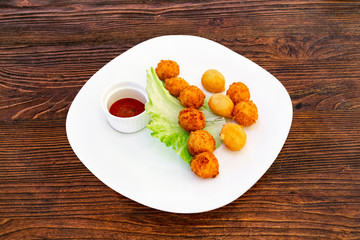 Cheese balls on a white plate with lettuce leaves and sauce