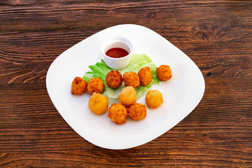 Cheese balls on a white plate with lettuce leaves and sauce