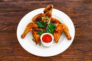 Grilled fried roast Chicken Tabaka on a plate on a wooden background, top view