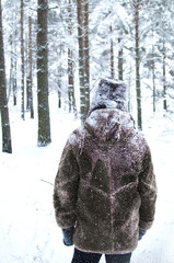 man walks through the winter forest in a warm fur coat and fur hat