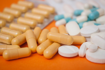 closeup of orange capsules and white pils on orange  background