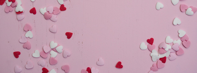 Panoramic website banner image with many tiny heart-shaped sugar sprinkles in red, white and pink with space for copy text or romantic love message for Valentine's Day on February 14th, flat lay