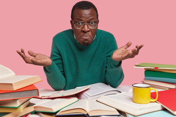 Picture of hesitant black man looks with clueless expression, cant choose topic for coursepaper,...