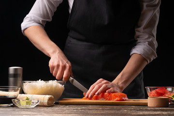 The chef cuts red fish, salmon for the preparation of Japanese sushi, rolls. The concept of delicious Japanese food, cooking, gastronomy, menus and recipe books