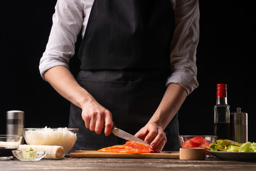 The chef cuts red fish, salmon for the preparation of Japanese sushi, rolls. The concept of delicious Japanese food, cooking, gastronomy, menus and recipe books