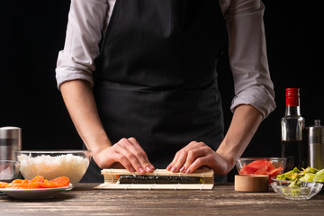 Obraz na płótnie Canvas A woman makes Japanese sushi rolls at home. Japanese food, and a recipe book menu.