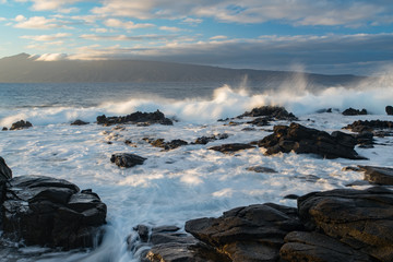 Waves breaking on a rocky shore just after a passing storm on the Hawaiian island of Maui at sunset.