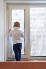 Little boy stands on windowsill and looks out window. Child is unrecognizable. Lonely childhood. Waiting for parents.