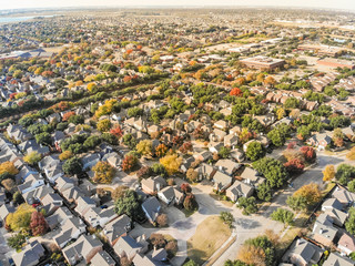 Aerial drone view urban sprawl in suburban Dallas, Texas during fall season with colorful leaves. Flyover subdivision with row of single-family detached houses and apartment complex