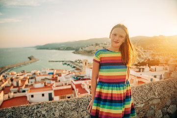 Little girl on the top of Peniscola, admiring amazing summer sunset, travel with children, wearing colorful dress