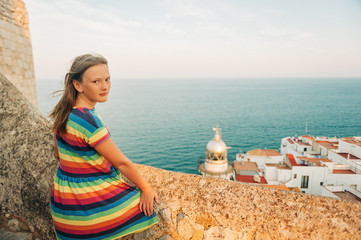 Fototapeta na wymiar Little girl on the top of Peniscola, admiring amazing summer sunset, travel with children, wearing colorful dress