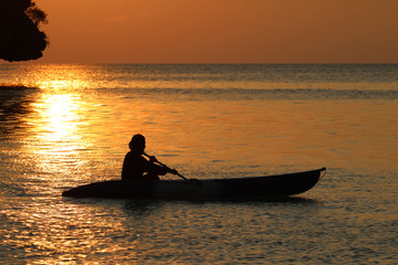 Asian man rowing a kayak near the beach with red sky sunset