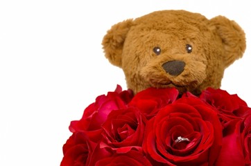 The bouquet of red roses that have silver diamond ring inside with blurred Teddy bear at the back for Valentine’s Day in 14 February of every year isolated on white background with space for text. 