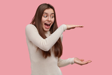 Happy overemotive young woman shows big size of recieved present, shares positive emotions with...