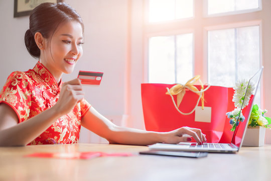 Happy Chinese Woman Wearing A Qipao Dress Traditional Or Cheongsam And Buying Online With A Red Credit Card. Online Shopping Website On Laptop