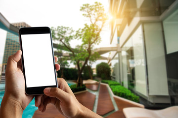 Hand holding white mobile phone with blank white screen  in cafe at the pool.