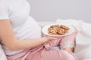 Fototapeta na wymiar Close up pregnant woman on a bed is holding chocolate cookies