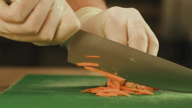 Chef is cutting vegetables by a knife - chopping carrots. Close-Up Slow Motion