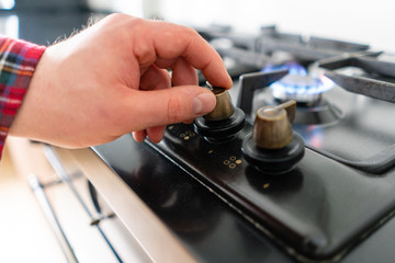 A man lighting the gas-stove with by means of automatic electric ignition. Modern gas burner and hob on a kitchen range. Dark black color and wooden Small kitchen in a modern apartment