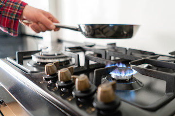 A man lighting the gas-stove with by means of automatic electric ignition. Modern gas burner and hob on a kitchen range. Dark black color and wooden Small kitchen in a modern apartment