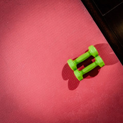 Naklejka premium Pink yoga mat and dumbbells lying on floor in gym