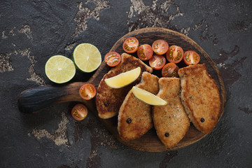 Rustic wooden serving board with fried fish cutlets made of pike fillet, flatlay on a brown stone background, studio shot