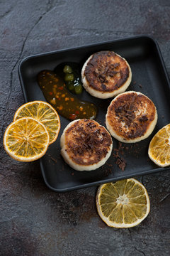 Cast-iron serving tray with cottage cheese pancakes on a cracked stone background, studio shot