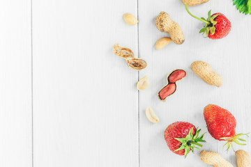 Strawberries and peanuts on white wooden background.