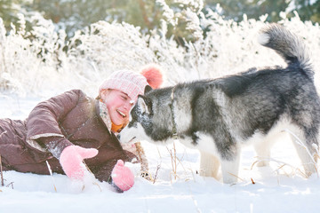 Siberian Husky dog and little girl child playing in a snowy winter forest