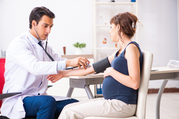 Obraz premium Young doctor checking pregnant woman's blood pressure